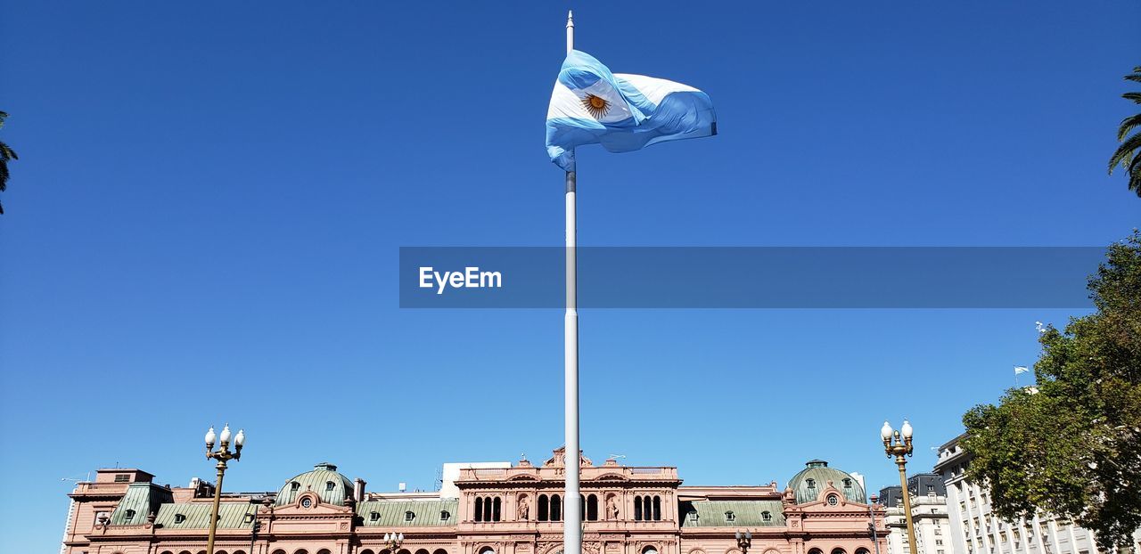 Low angle view of flag against building against clear blue sky