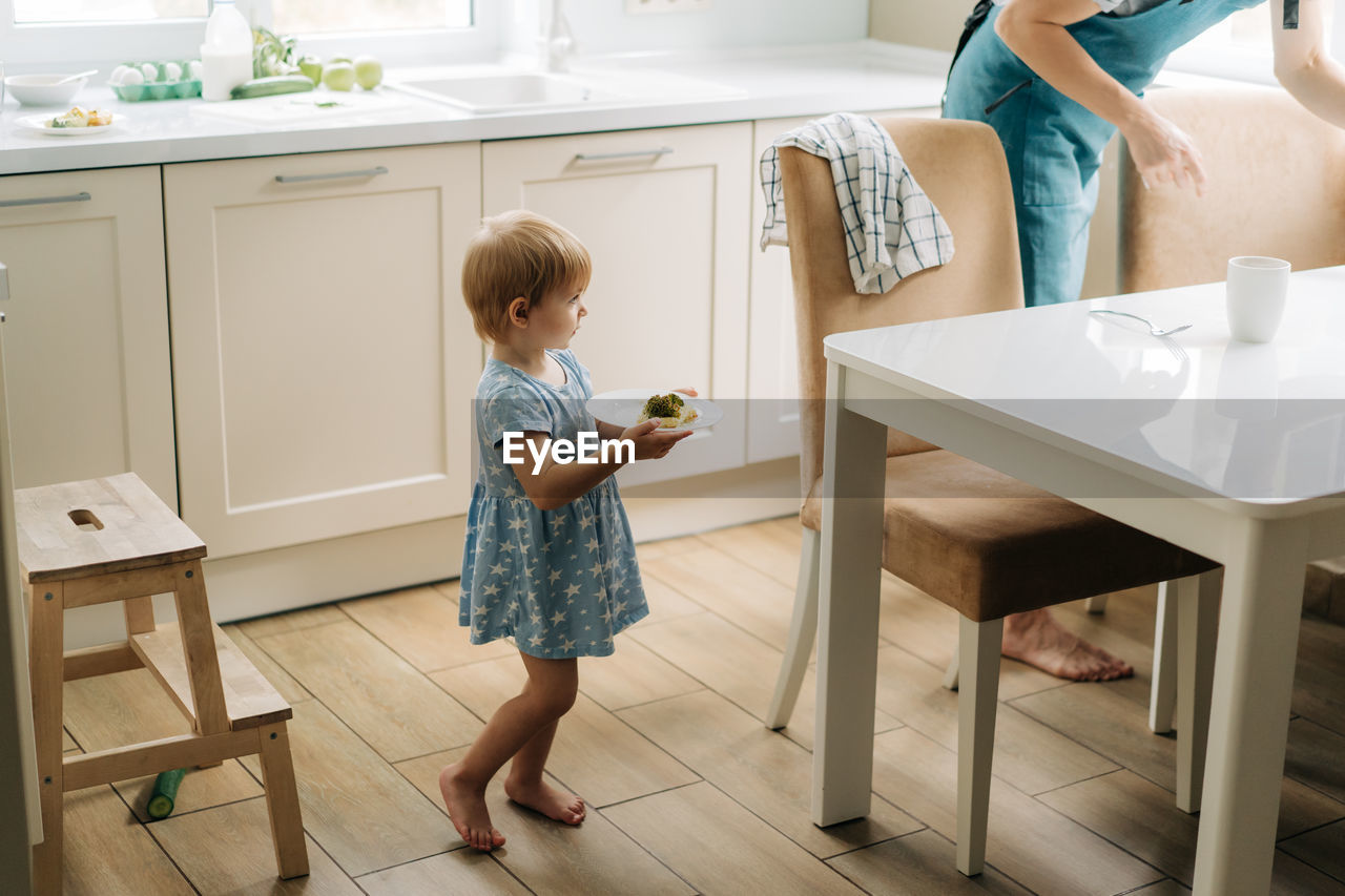 Mom and little daughter are setting the table for dinner at home in the kitchen.