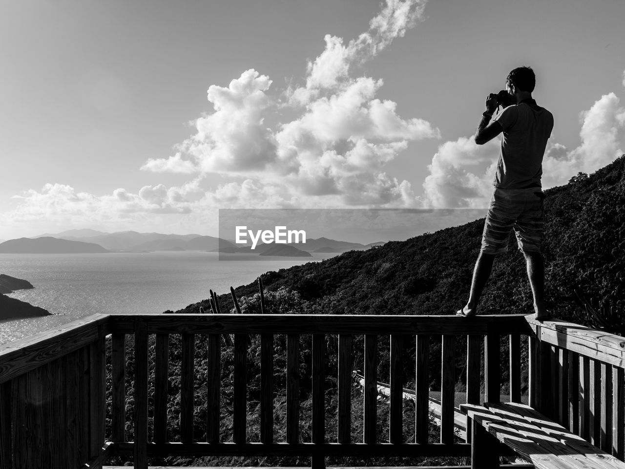 Man photographing through camera while standing on railing at observation point