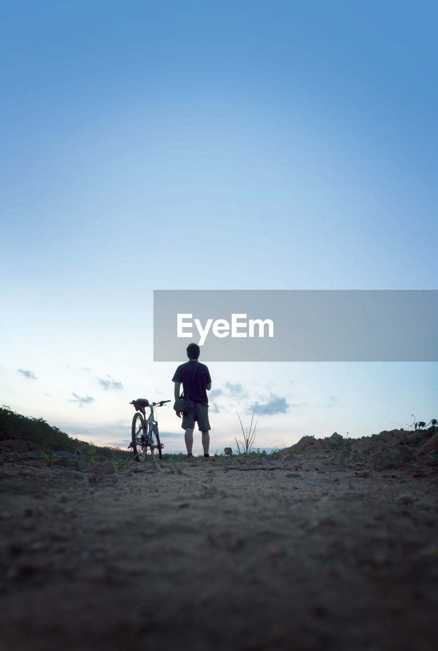 Rear view of man with bicycle on road against sky