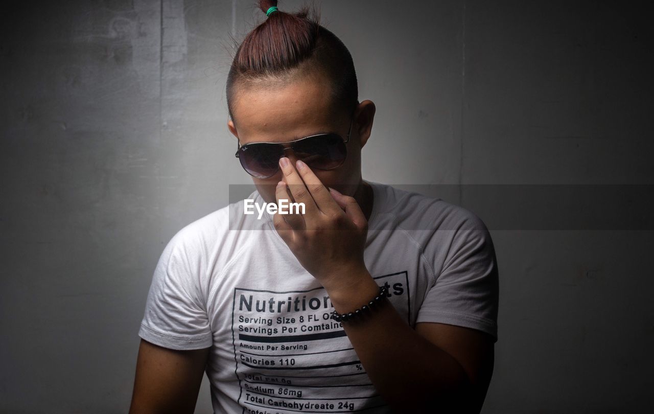 MAN WEARING SUNGLASSES STANDING AGAINST WALL