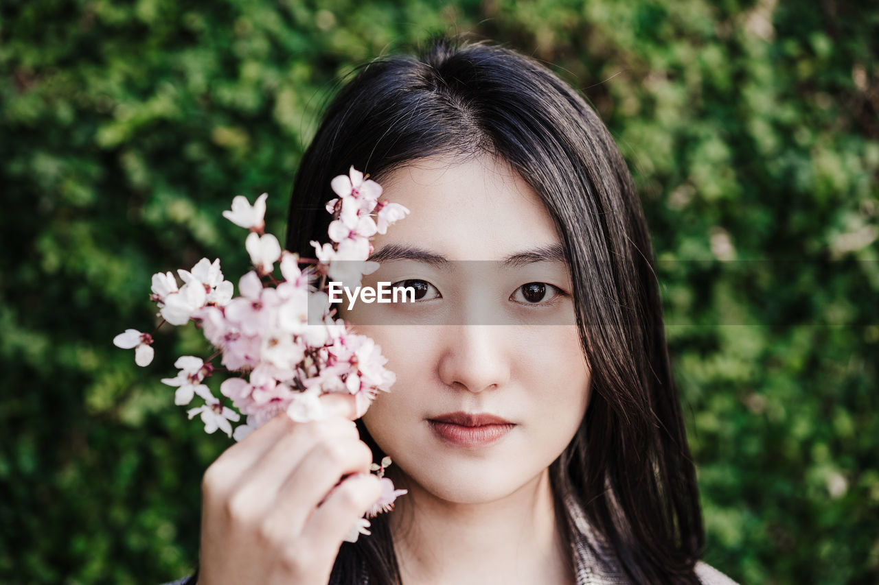 Portrait of beautiful chinese asian woman holding almond tree flowers. springtime outdoors