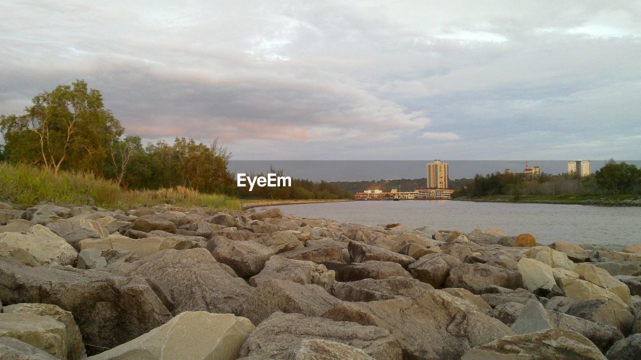 SURFACE LEVEL OF CALM BEACH AGAINST CLOUDY SKY