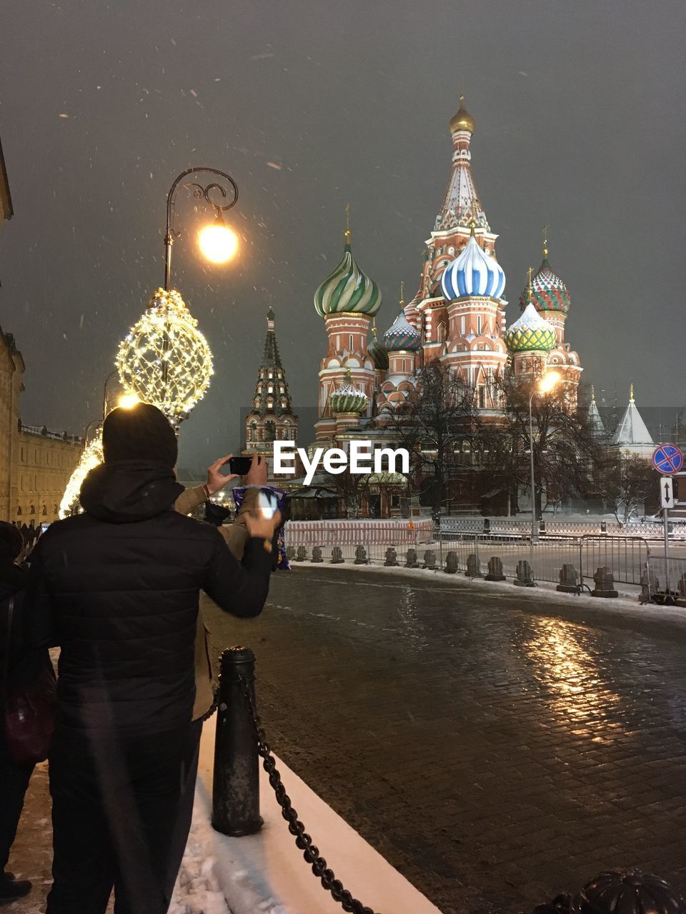 REAR VIEW OF WOMAN PHOTOGRAPHING ILLUMINATED CATHEDRAL IN CITY