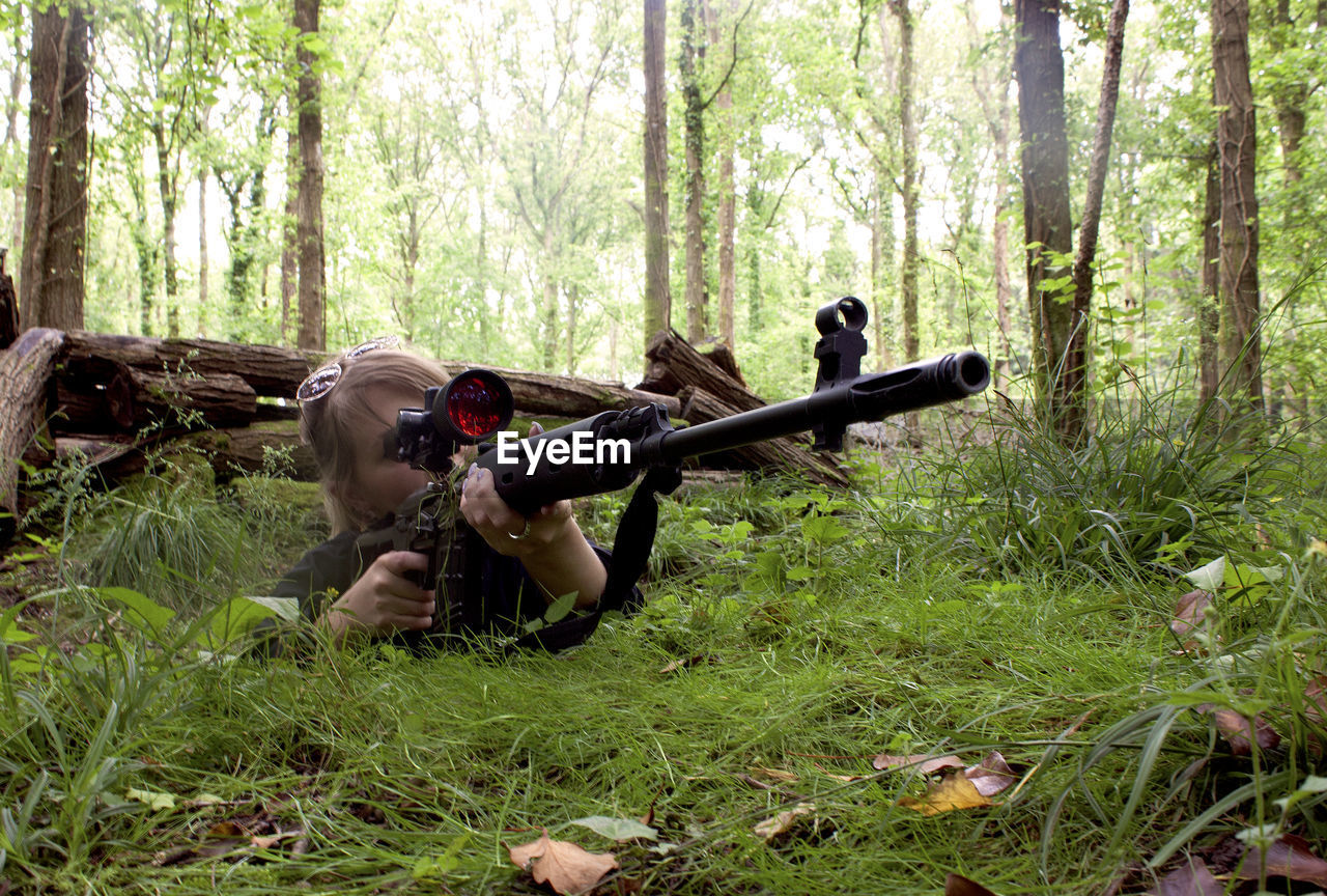 Woman lying down behind a rifle in a forest
