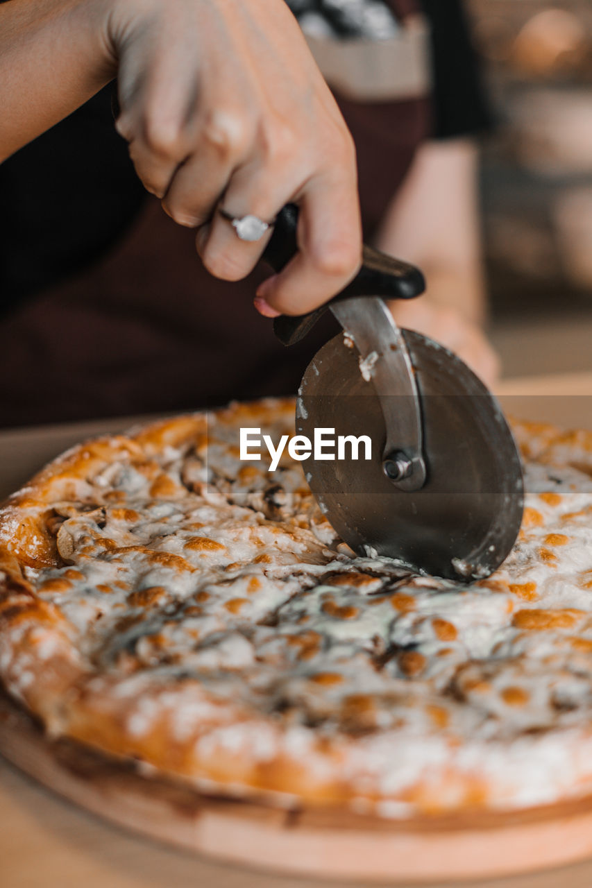 CLOSE-UP OF HAND HOLDING PIZZA