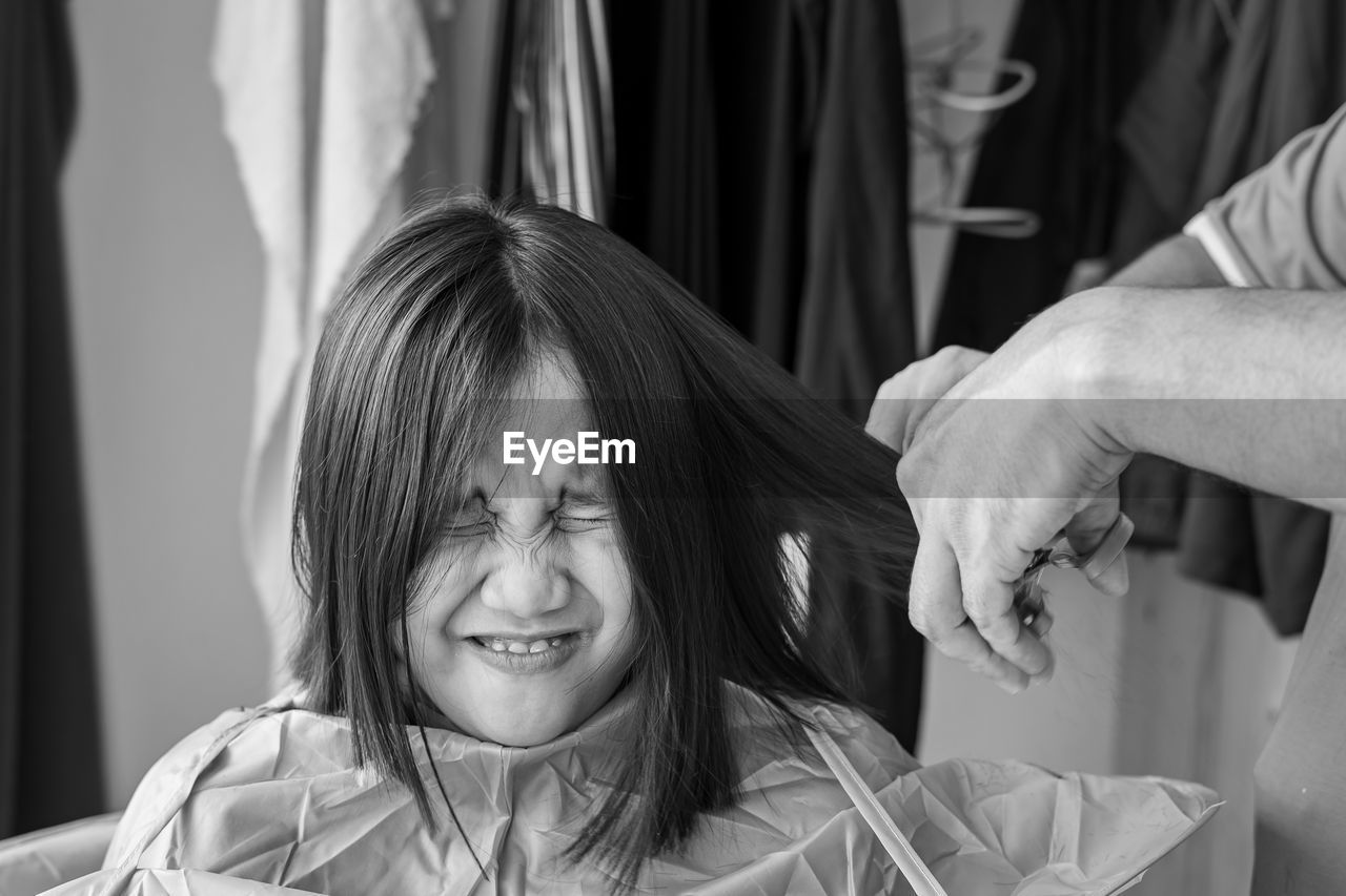 Asian young girl with funny expression is getting haircut at home. monochrome, black and white.