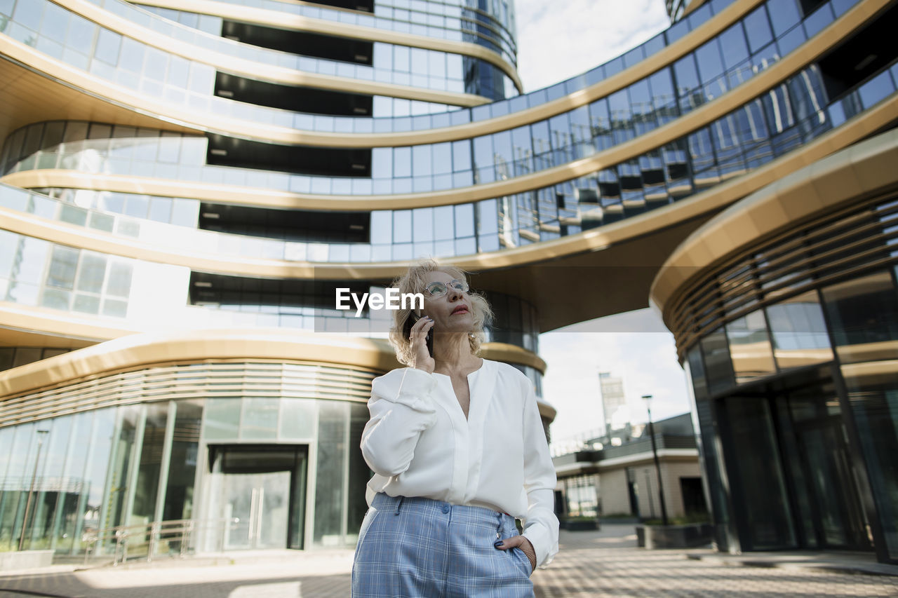 Senior businesswoman talking on mobile phone in front of office building