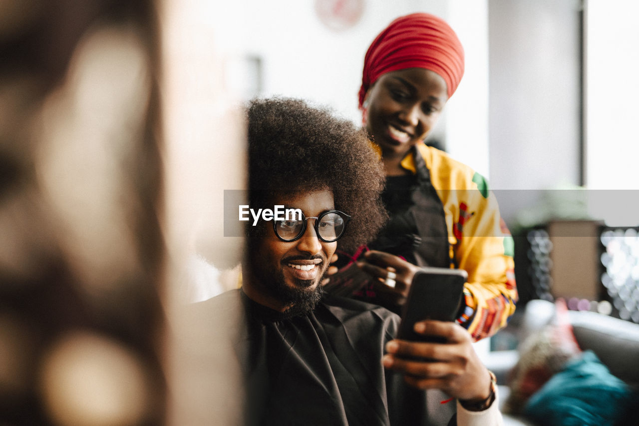 Smiling male customer taking selfie with female barber at hair salon