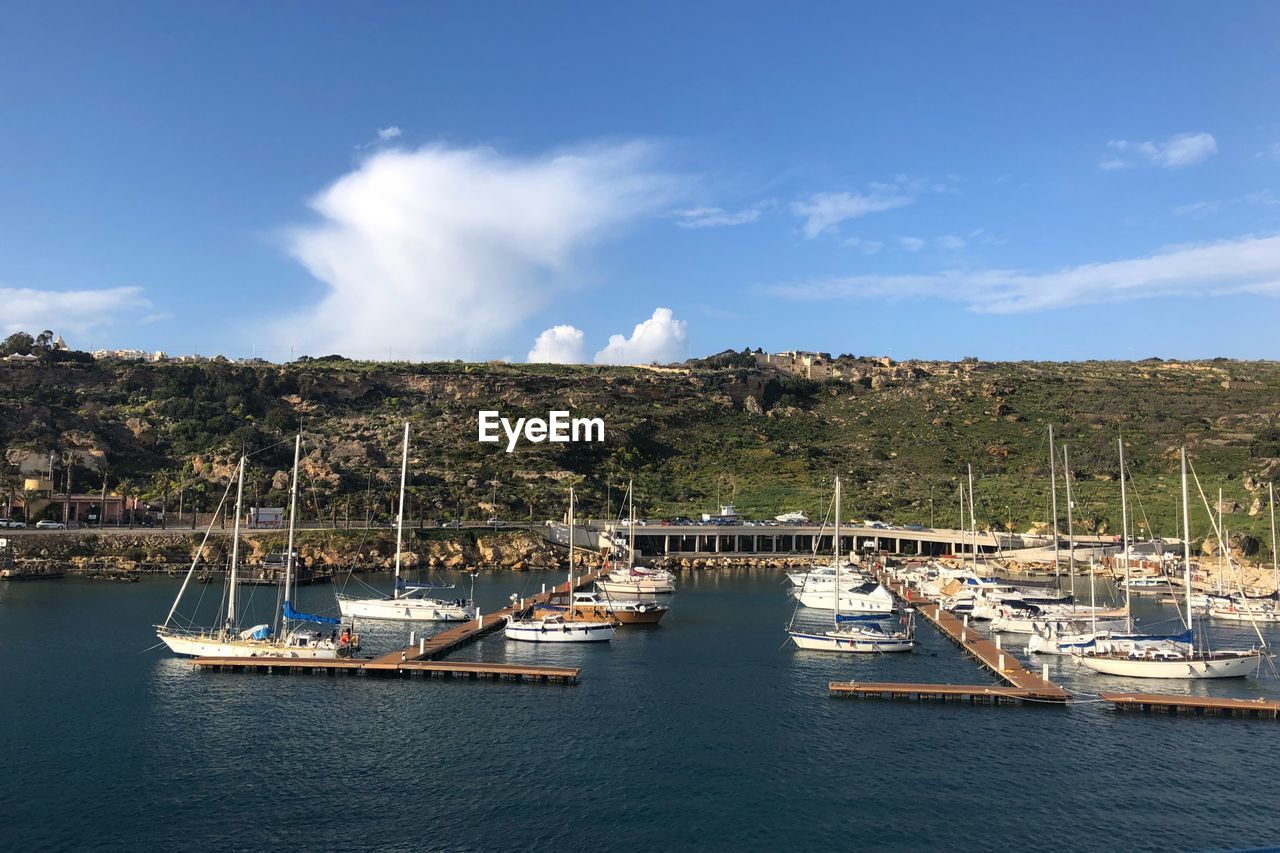 SAILBOATS MOORED ON HARBOR AGAINST SKY