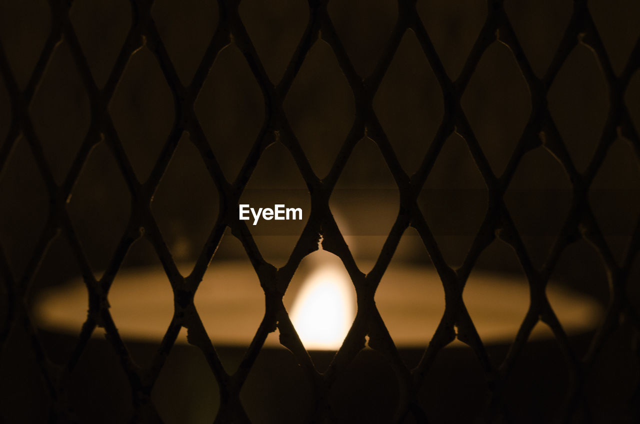Lit candle seen through metal grate