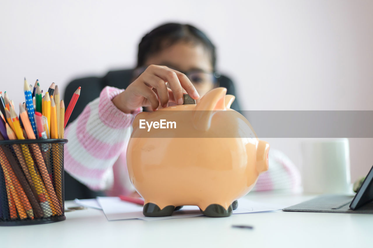 Girl inserting coin in piggy bank on table