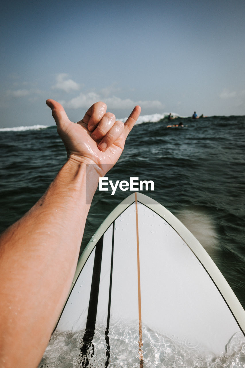 Cropped image of hand gesturing against in sea against sky