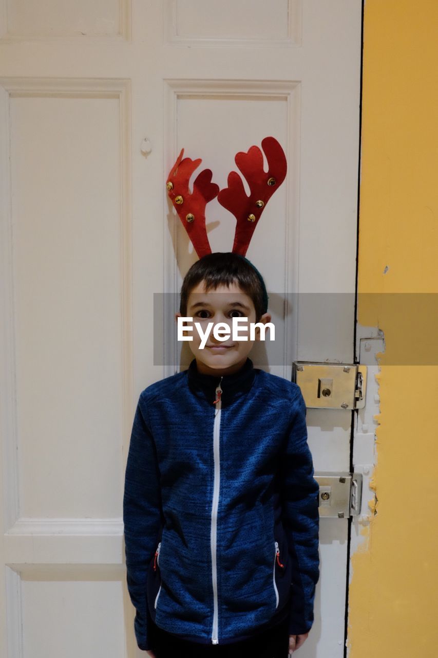 Portrait of smiling boy with christmas antler standing against door