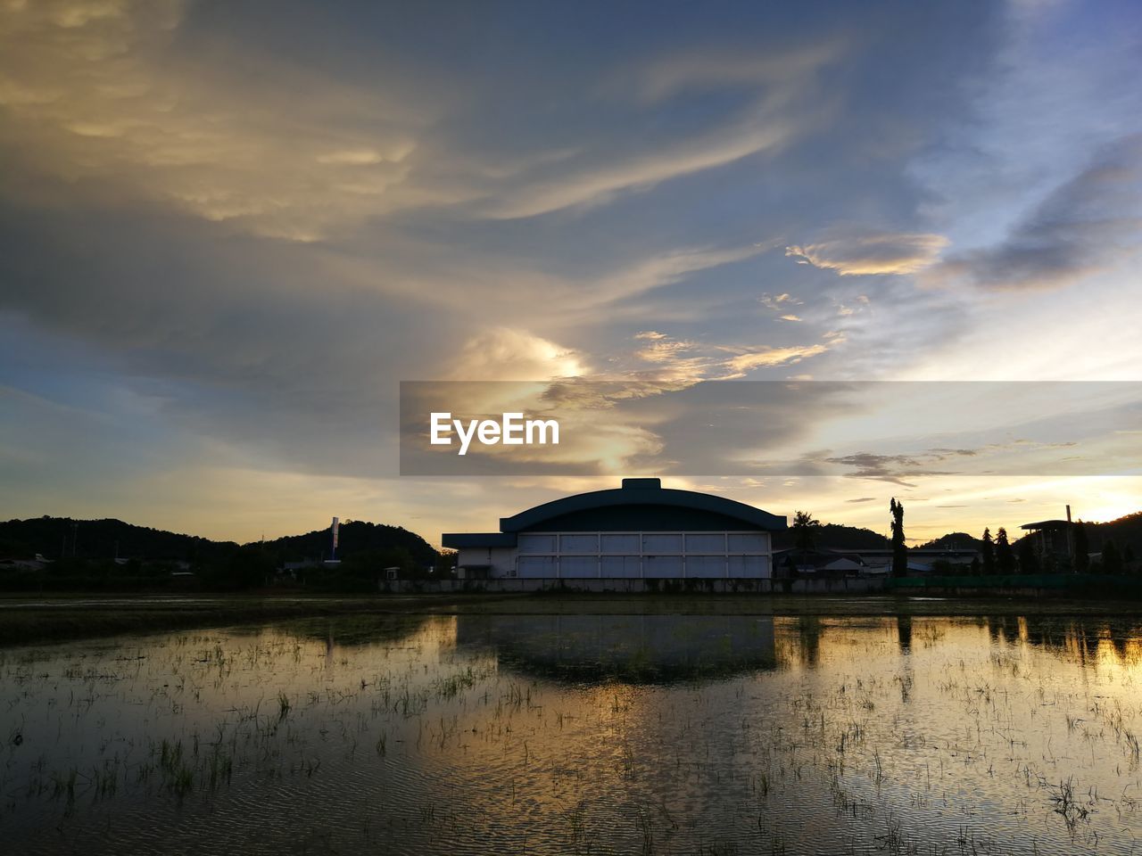 BUILDING BY LAKE AGAINST SKY AT SUNSET