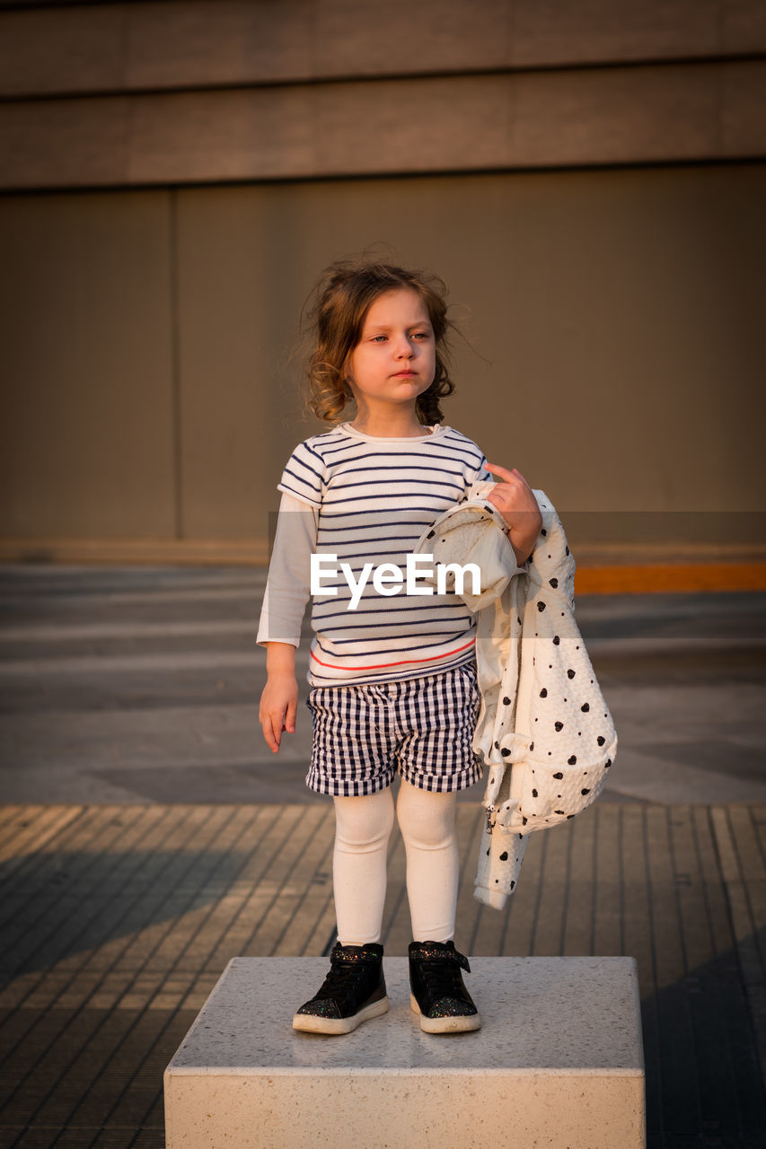 Cute girl looking away while standing on seat