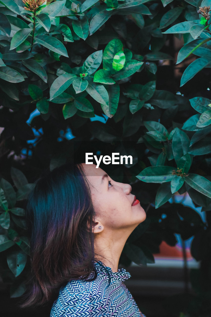 Side view of mid adult woman looking away while standing by plants in park