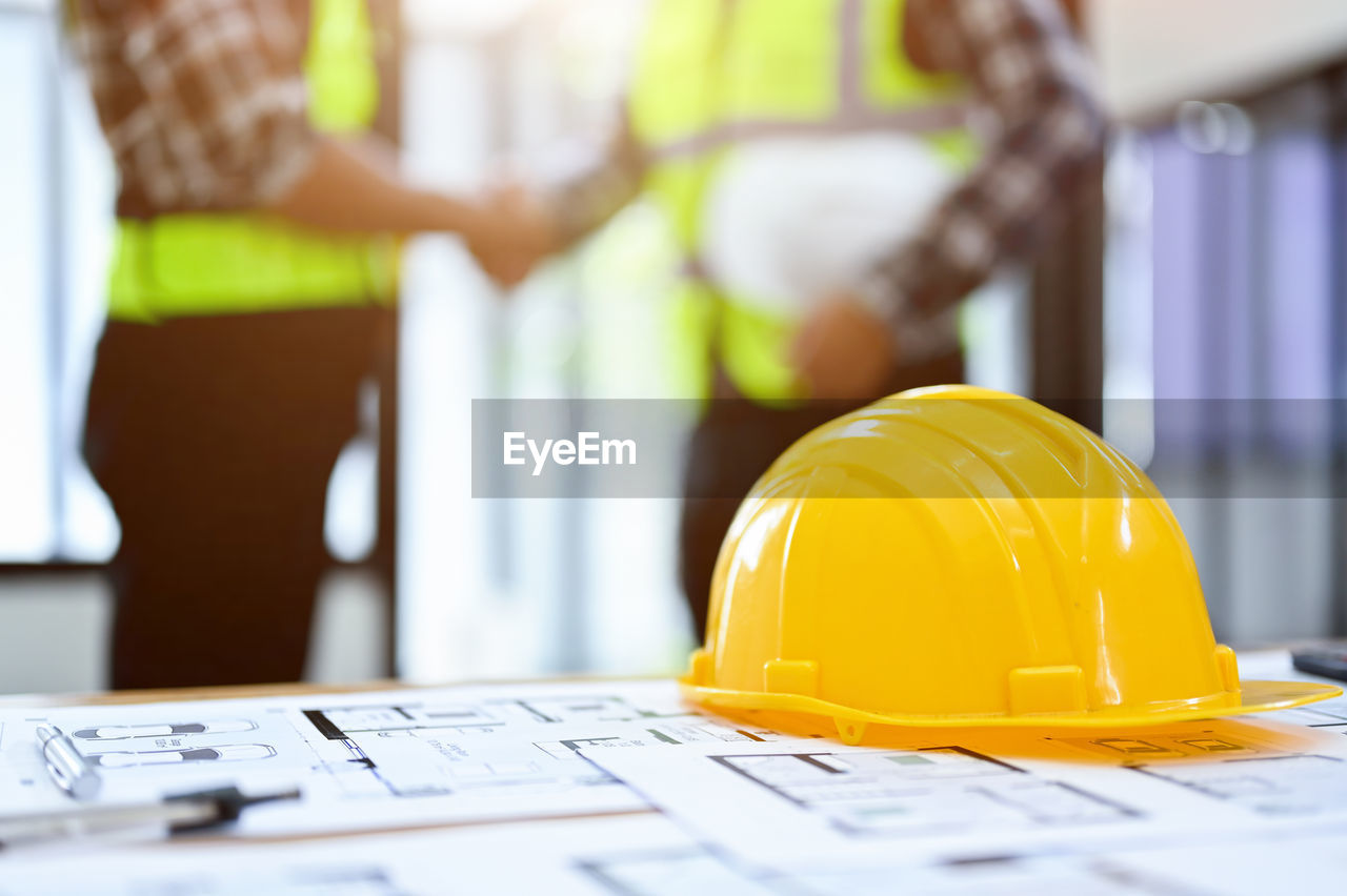 hard hat, construction industry, occupation, headwear, helmet, working, industry, business, construction worker, adult, planning, plan, construction site, hat, yellow, protection, engineering, building contractor, blueprint, men, manual worker, protective workwear, business finance and industry, work helmet, reflective clothing, cooperation, professional occupation, clothing, teamwork, security, indoors, technology, architecture, personal protective equipment, person, document, white-collar worker, communication, development, occupational safety and health, place of work, equipment, office, businessman, construction, computer, expertise, paper