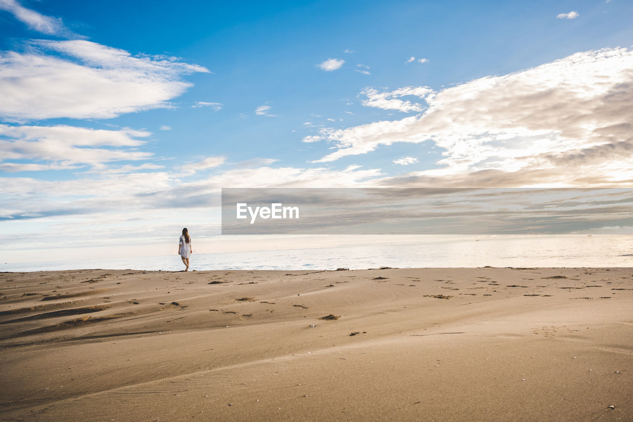 Mid distance view of woman walking on shore at beach against sky