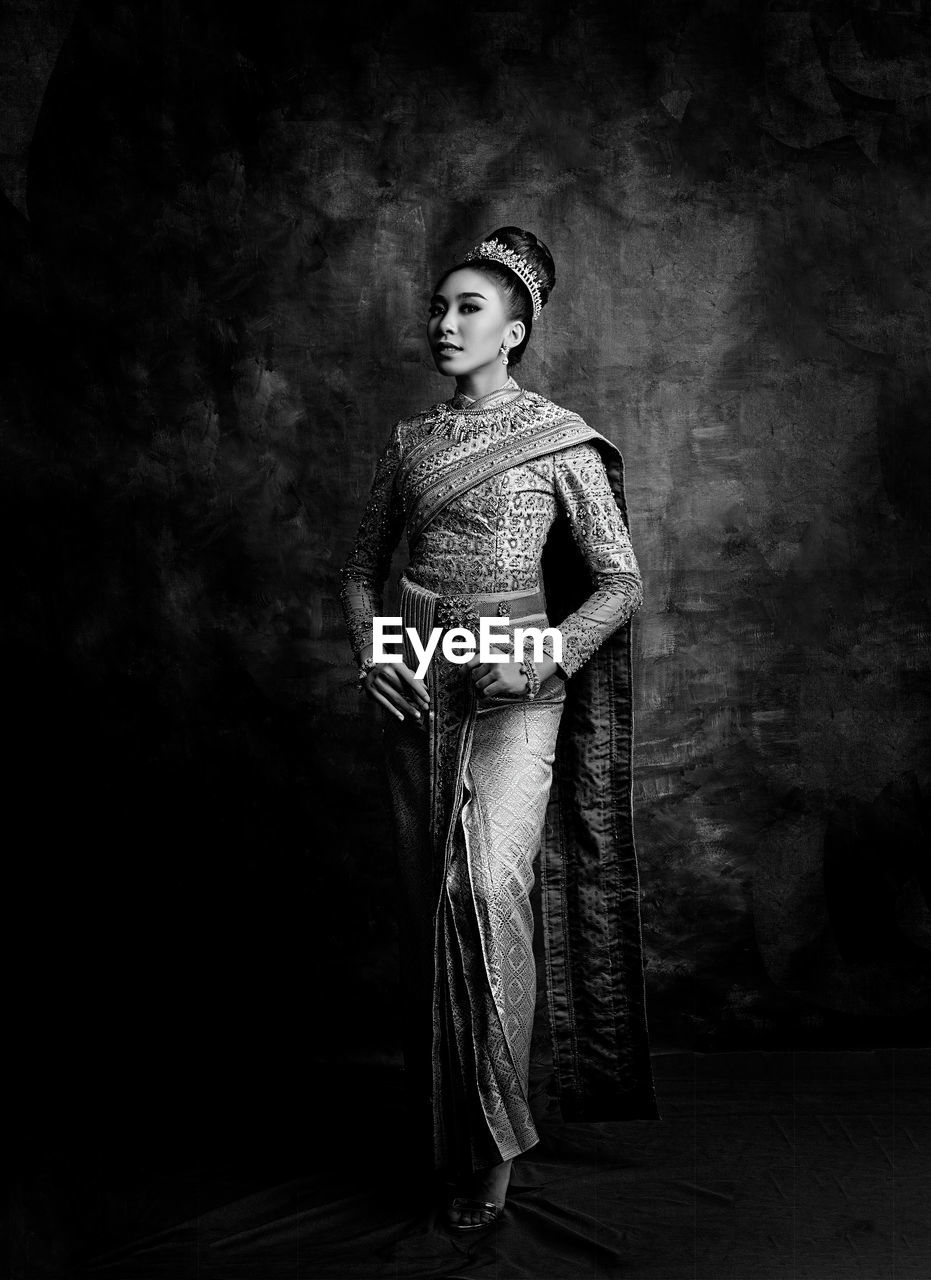 Teenage girl in traditional clothing standing against backdrop