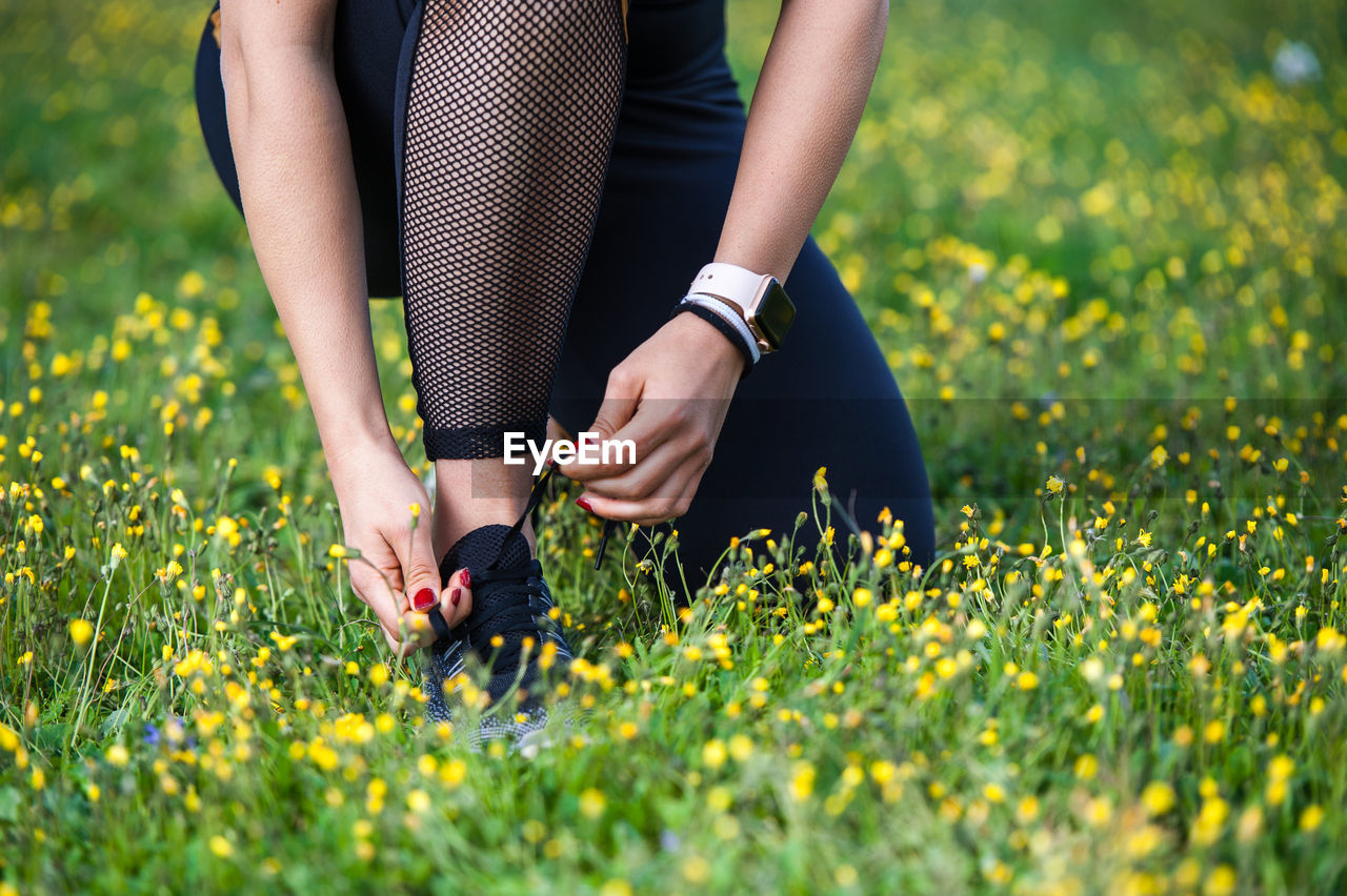 Low section of woman tying shoelace on grassy field