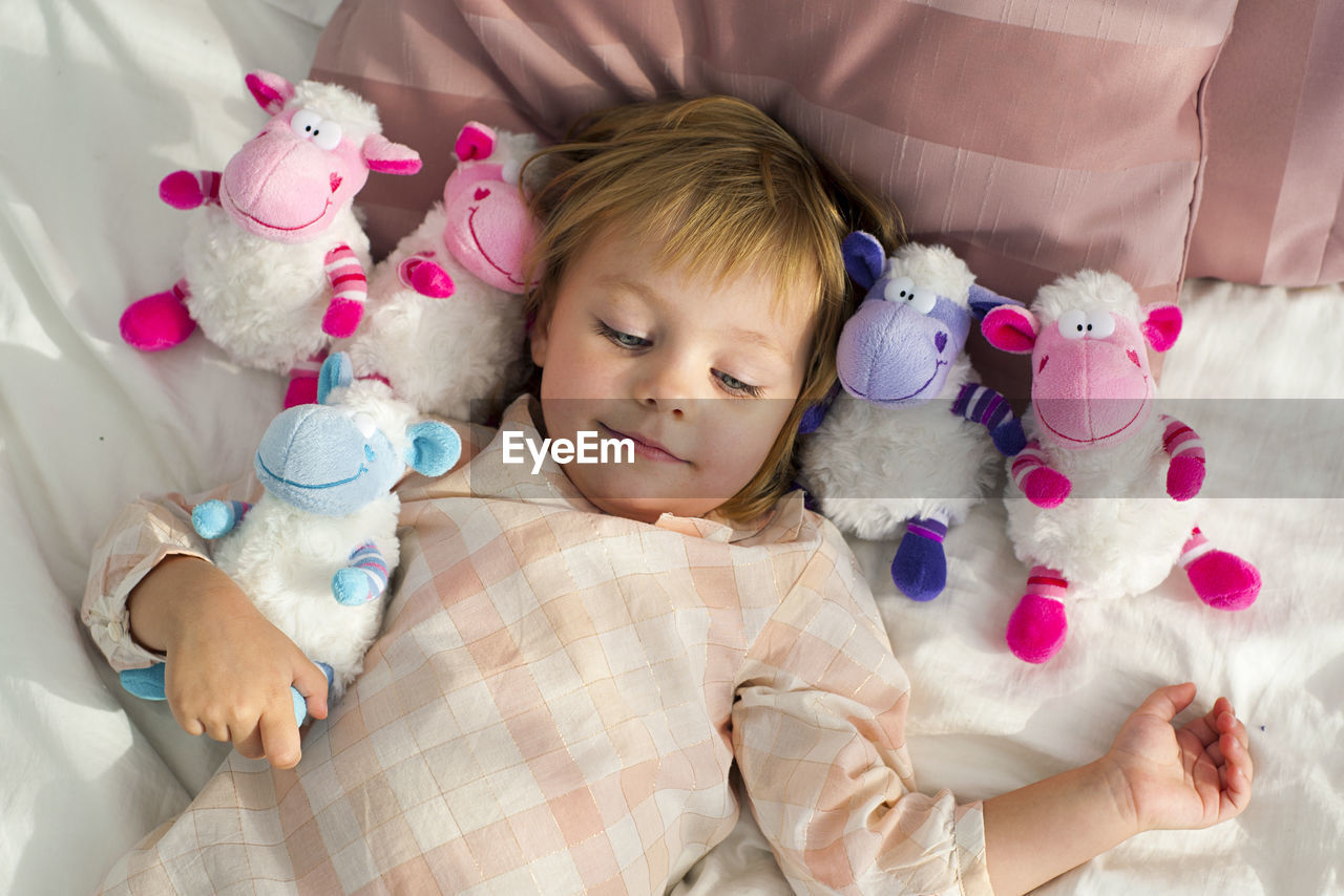 Smiling girl with toys lying on bed at home