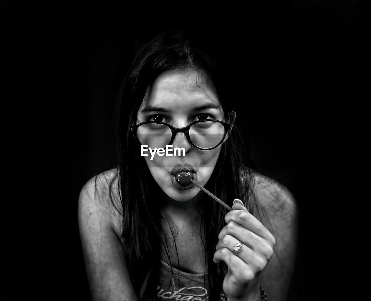 Portrait of beautiful young woman eating lollipop against black background