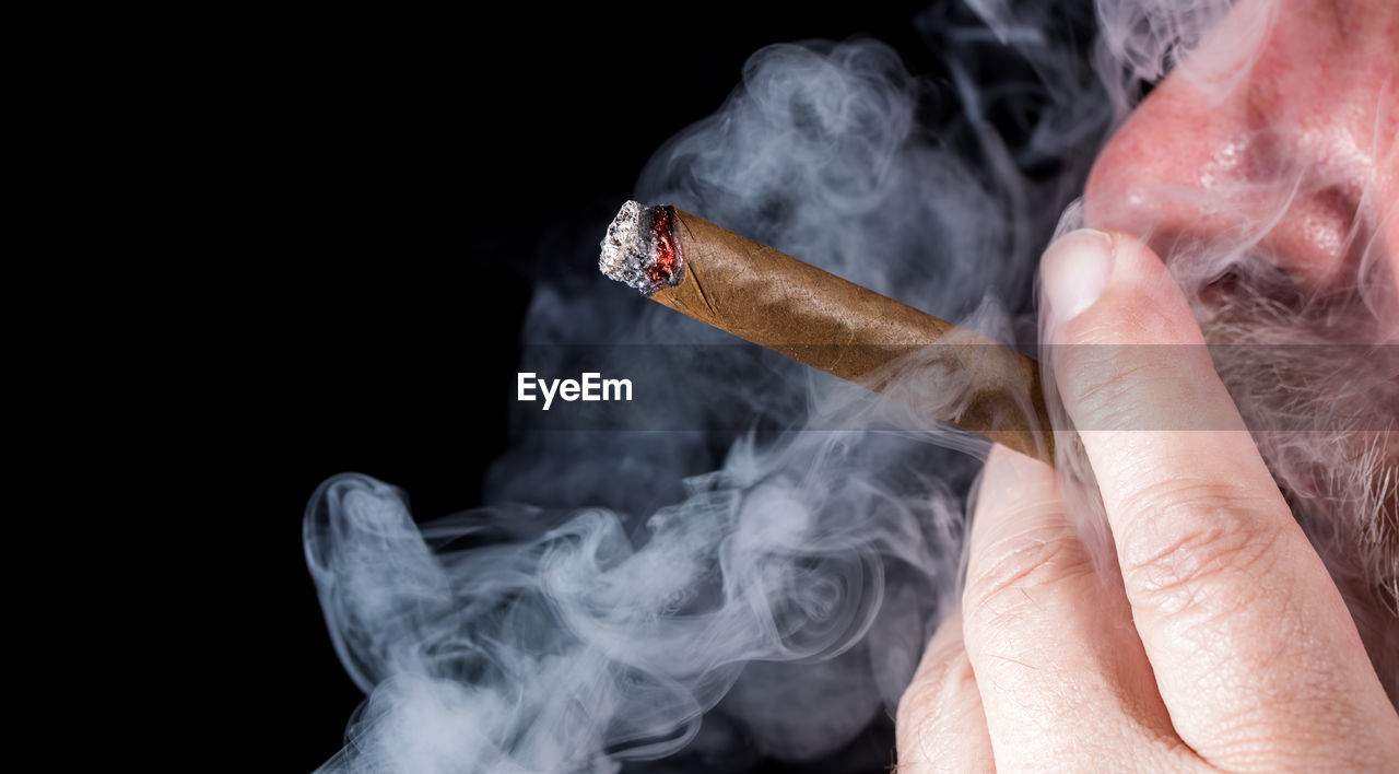 Man smoking cigar against black background