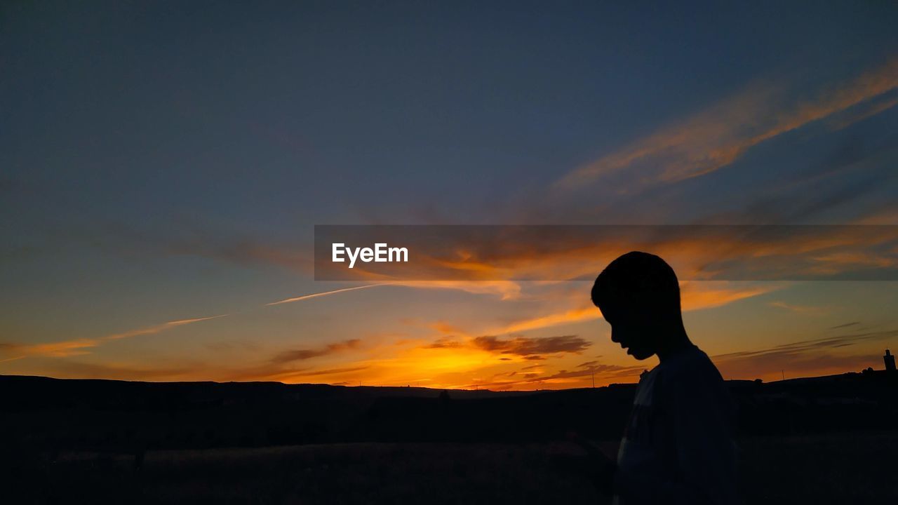 Silhouette man standing against orange sky during sunset