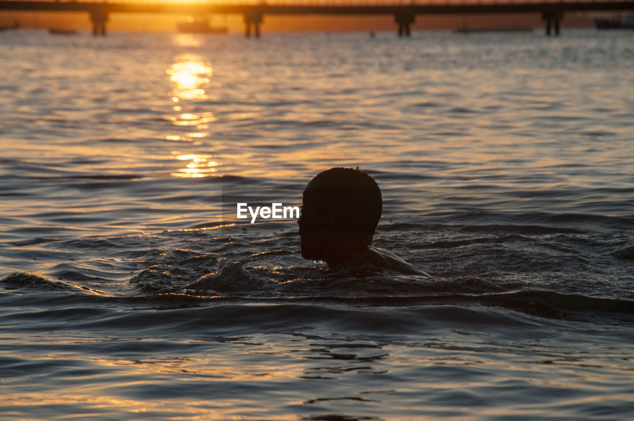 Side view of silhouette boy swimming in sea during sunset