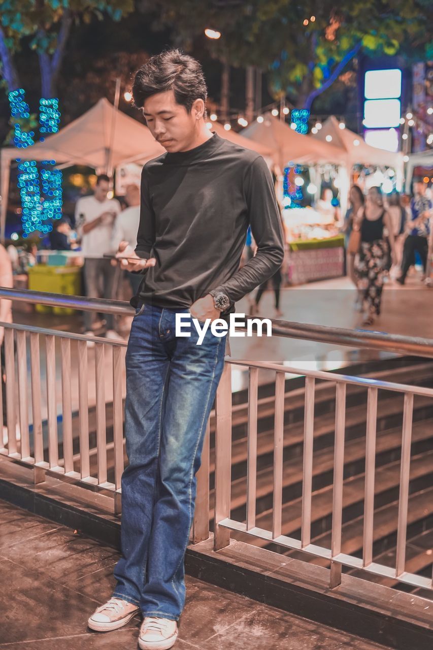 Young man using phone while leaning against railing by staircase