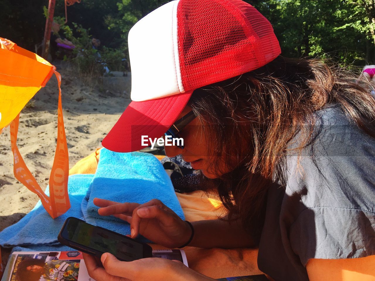 MIDSECTION OF WOMAN USING MOBILE PHONE WHILE SITTING IN HAT