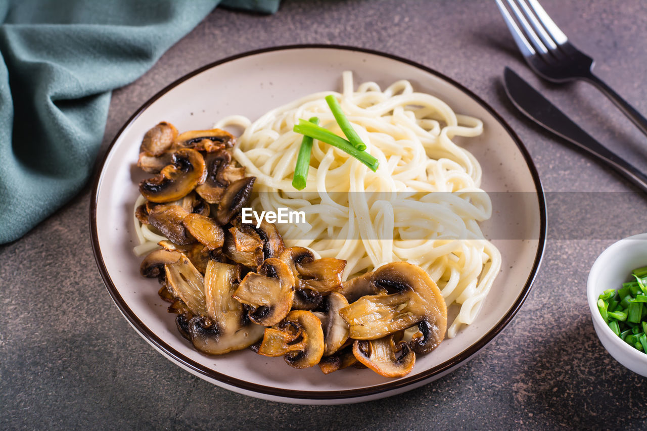 Udon noodles, fried champignons and greens on a plate on the table