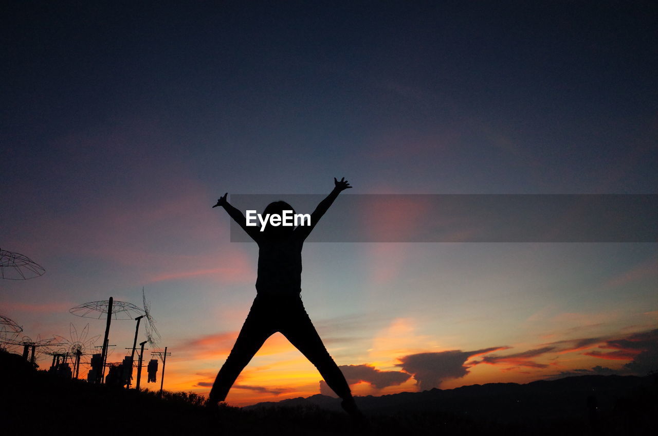 Silhouette girl jumping on field against orange sky during sunset