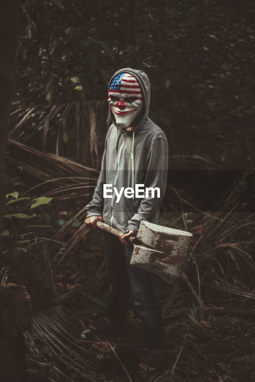 Man in mask holding spade in forest