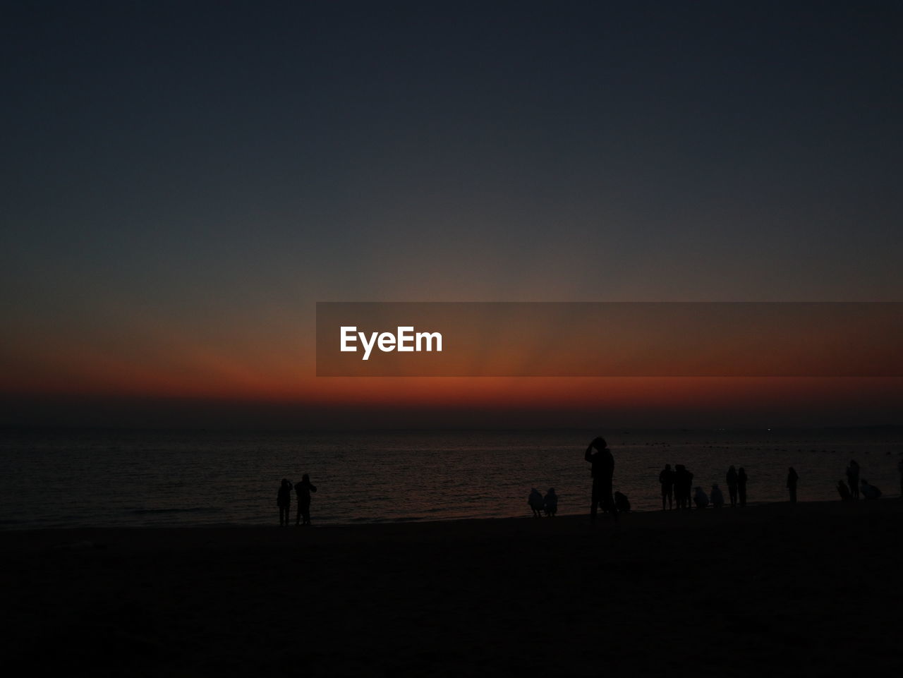Silhouette people on beach against sky during sunset