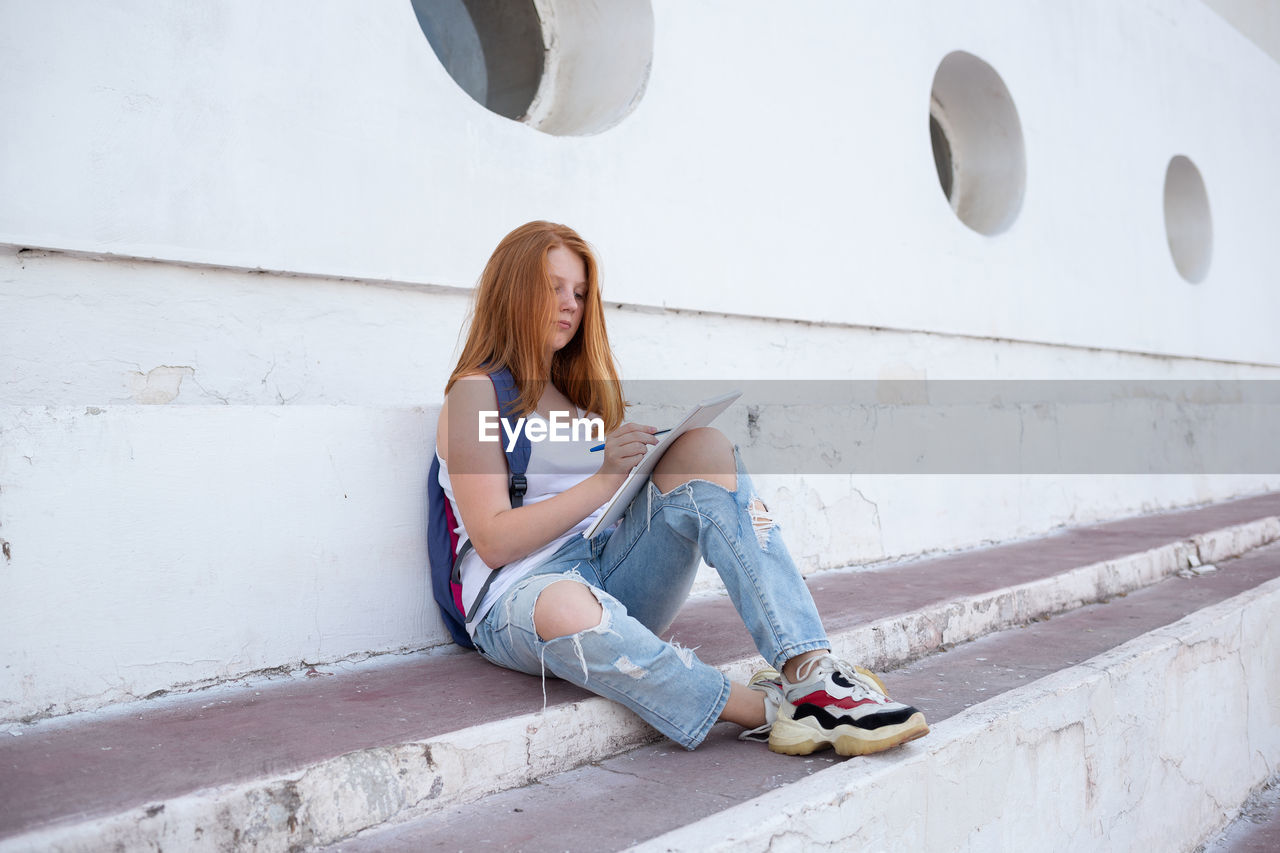 Full length of young woman sitting against wall