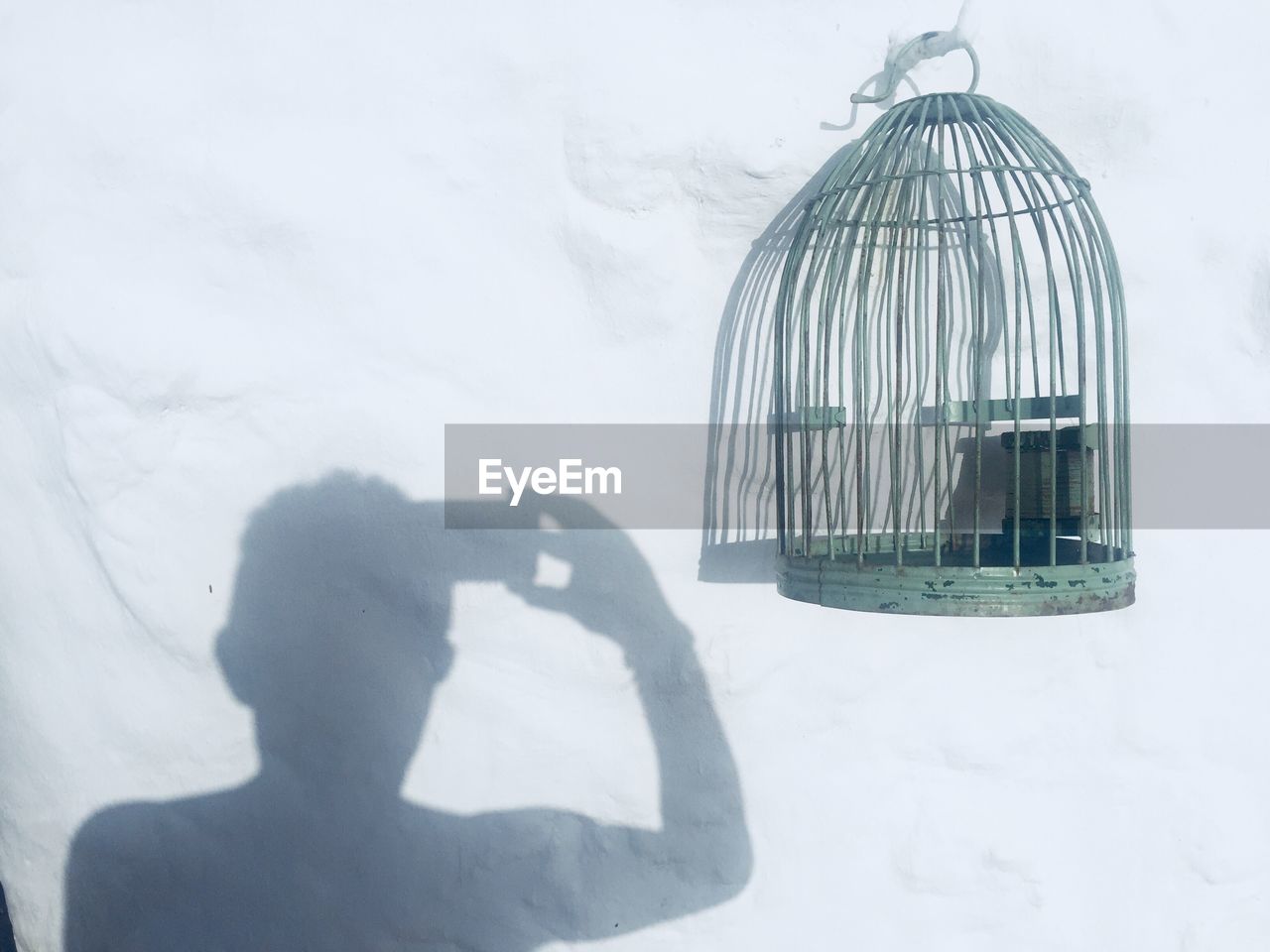 Shadow man photographing cage hanging on wall