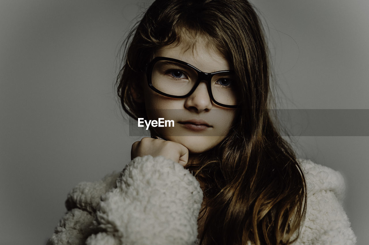 Close-up portrait of cute girl wearing eyeglasses against gray background
