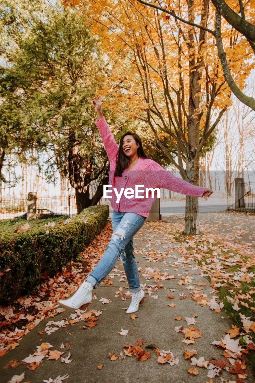 Full length of happy young woman with arms outstretched autumn leaves