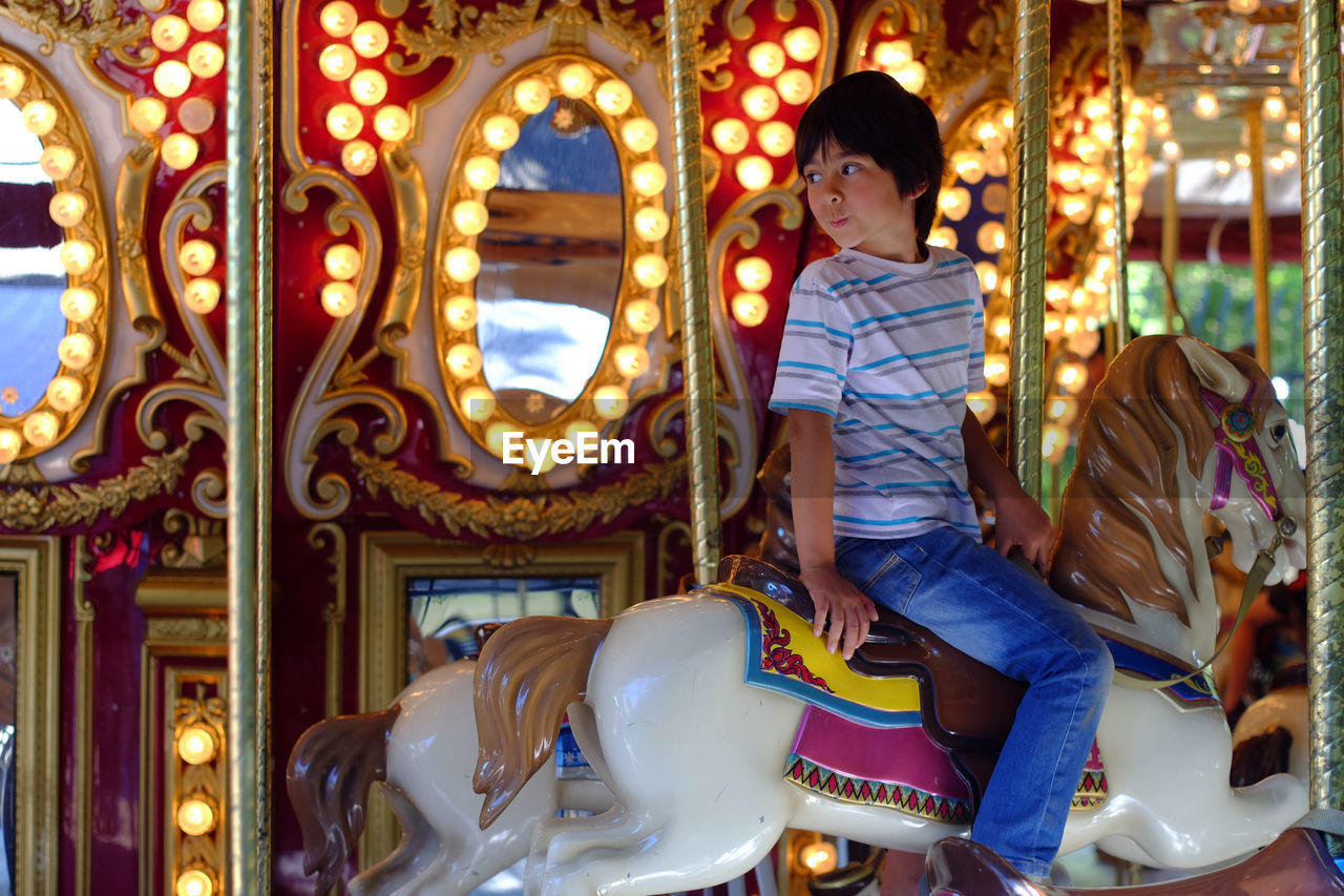 Boy looking away while sitting on carousel horse