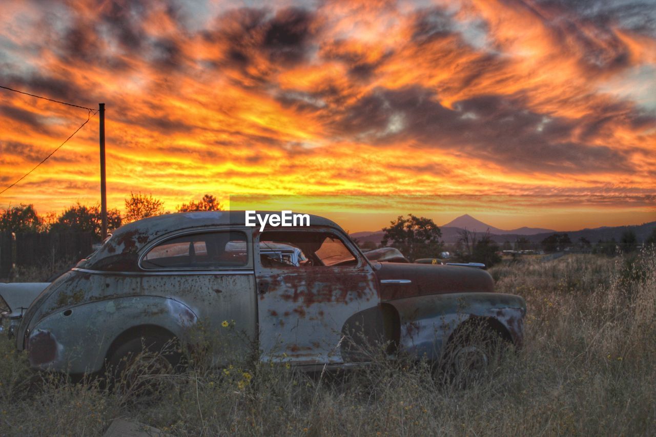 VIEW OF ABANDONED CAR ON FIELD DURING SUNSET
