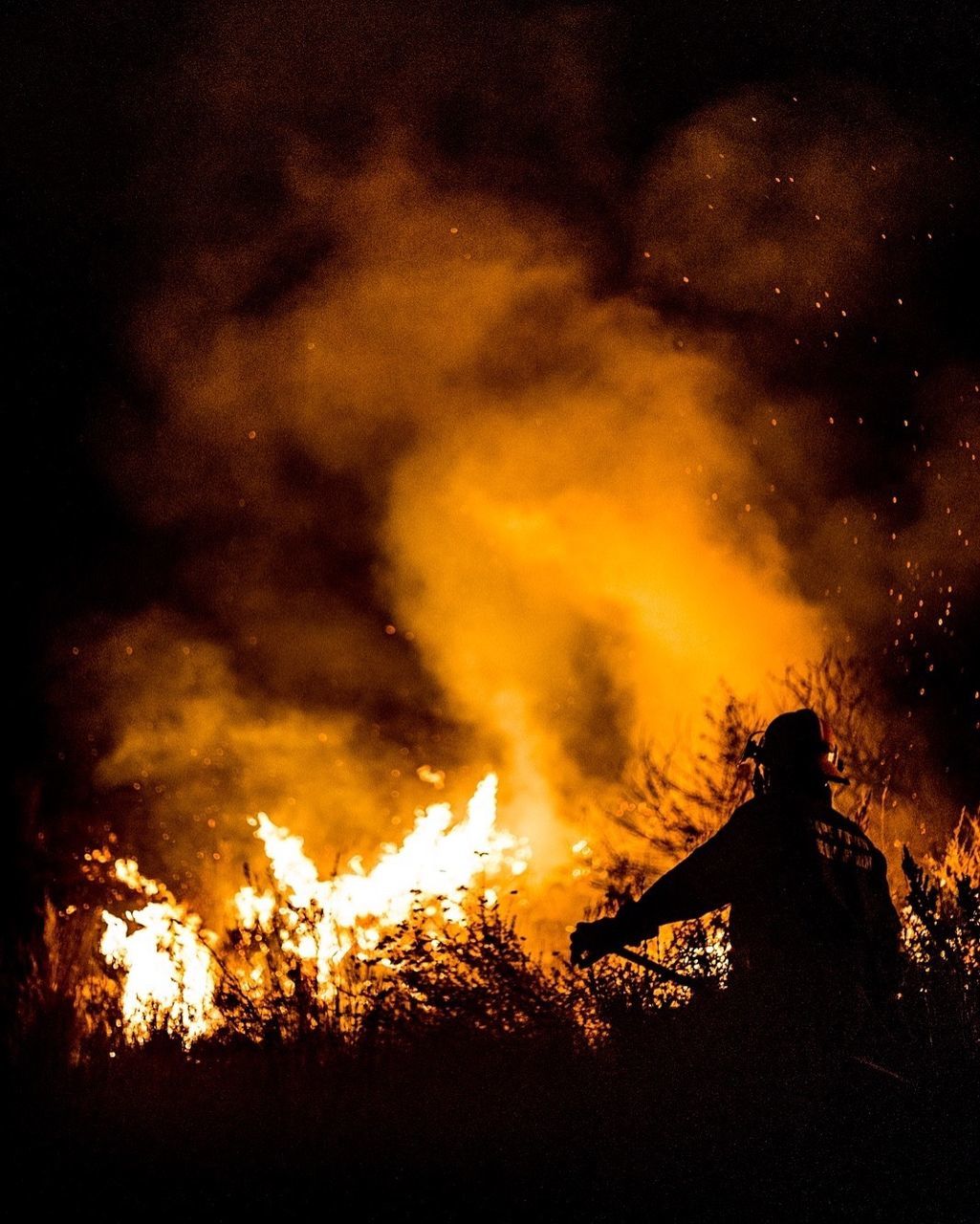 Firefighter standing against fire in forest at night