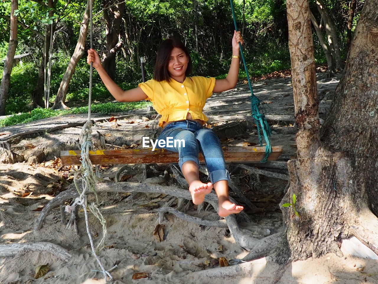 Portrait of smiling woman sitting on swing hanging from tree trunk