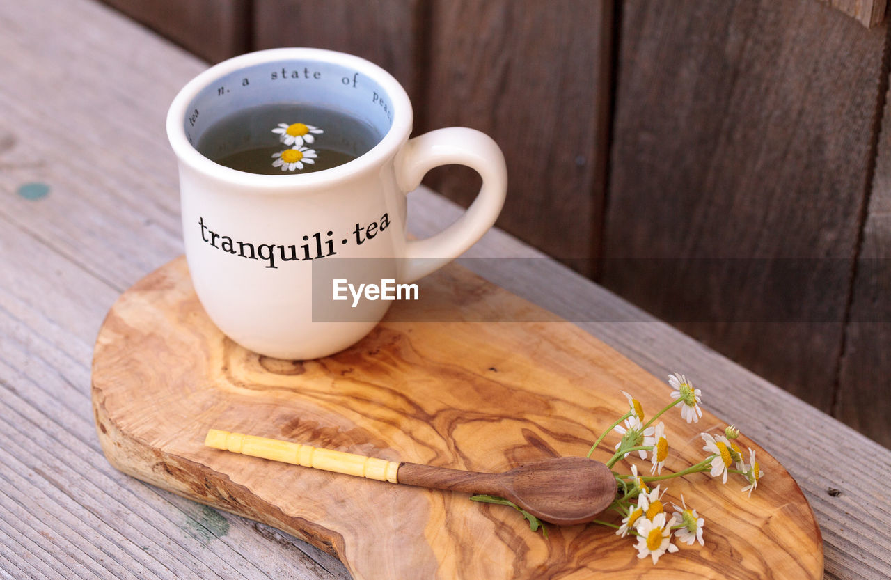 High angle view of chamomile tea with daisy flowers on cutting board