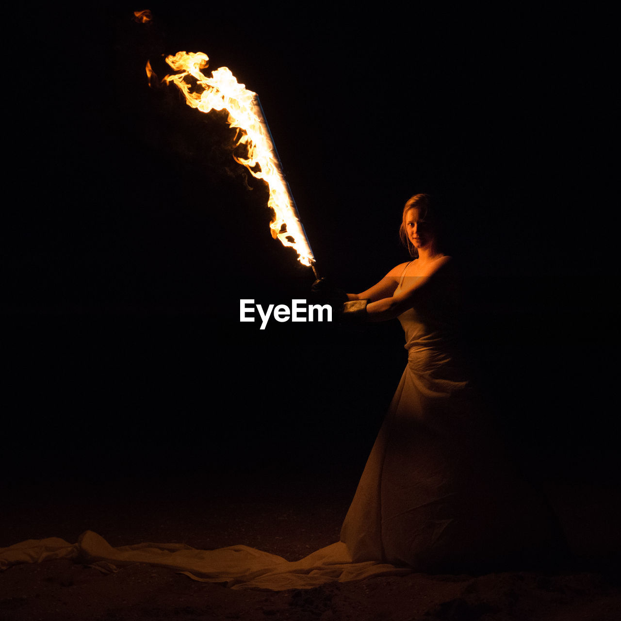 Woman standing and holding fire torch against black background