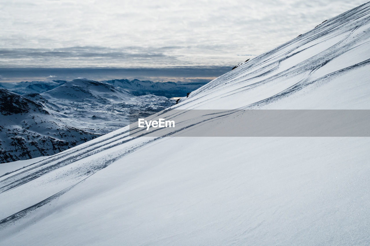 Snow covered mountain with ski tracks against sky 