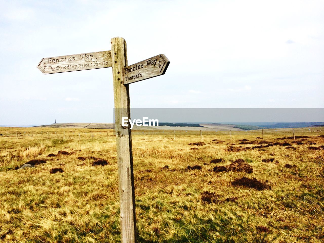 Road sign on grassy field against sky