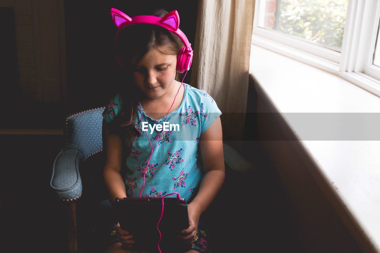 High angle view of girl using digital tablet while listening to pink headphones at home