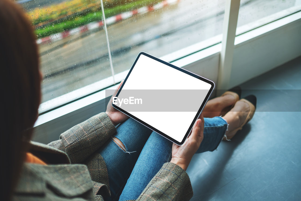 Mockup image of a woman holding and using digital tablet with blank white desktop screen